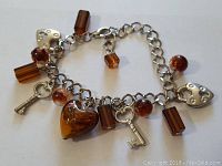 Silver toned charm bracelet with amber-colored and silver charms arranged to show variety of beads and keys.