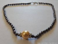 Full view of the necklace showing the grey pearl chain and larger cream pearl with rhinestone spacers at the center, laid out flat.