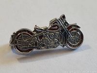 Close-up view of a metal vintage motorcycle pin showing detailed wheels, engine, and seat design.