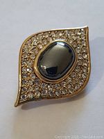 Front view of gold-toned brooch with oval hematite center and rhinestone border.