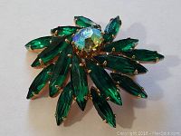 Front view of the gold-toned floral brooch with green stones arranged as petals and central iridescent stone.
