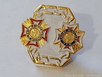 Front view of gold-tone Veterans of Foreign Wars Ladies Auxiliary pin with red, black, and gold enamel detailing and dual insignia, mounted on a decorative gold backing with chain motif edges.