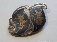 Front view of the Siam sterling silver pin showing two black curved sections with engraved traditional Thai figures and decorative silver edges.