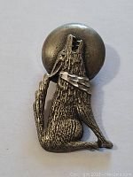 Front view of silver-toned metal button cover depicting wolf howling at moon.