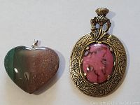 Front view of zoisite heart pendant and rhodonite oval pendant showing gemstone colors and metal frame details