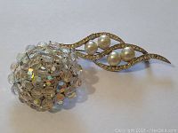 Front view of round Aurora Borealis crystal brooch and gold-tone leaf brooch with pearls.