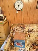 Clock mounted on wood panel wall above sofa, punch bowl set box on sofa