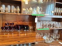 Dropdown shelf with Luminarc ruby red sherbet bowls and tumblers on clear bases; open shelf with rows of Capri Crystal clear stemware