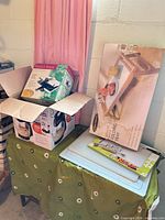 Lot overview showing opened box with mixer base/attachments, pizzelle baker box, folding tray box, cutting boards and utensil set