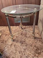 Full view of round glass side table showing top, legs, stretcher and flooring reference