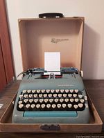 Typewriter inside open tan case showing full keyboard and paper in platen