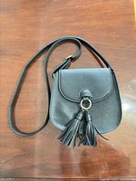 Front view of black faux leather crossbody bag with tassels and strap