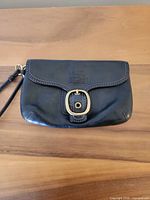 Front view of black leather Coach wristlet with buckle flap
