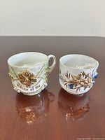 Front view of both porcelain moustache cups showing relief decoration and inscription