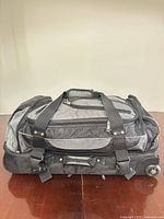 Side view of Roots black/gray rolling duffel showing wheels, exterior pockets and carry handles
