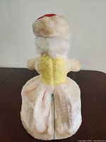 Back view of plush doll showing faux-fur body, yellow panel and zipper