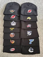 All 13 black NHL team beanies laid out in two columns showing embroidered logos