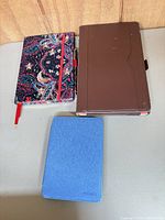 Top view of notebook with pen, brown tablet folio and blue Kindle case