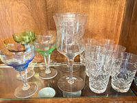 Group view showing all glasses: colored rim coupes, etched goblet, cut tumblers