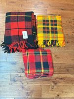 Three wool plaid throw blankets folded on floor