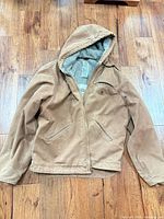 Front view of Carhartt brown hooded jacket laid flat showing pockets and zipper