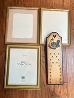 Overview of three gilt frames and chicken plaque on wood floor