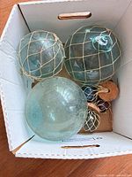 Box containing six glass fishing floats of various sizes and colors