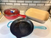 All three cookware pieces together: turquoise skillet, red sauté pan with lid, gray roasting dish