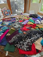 Overview of mixed scarves, bandanas and beaded shawl spread on table