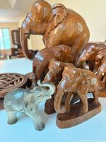 Group view showing large wooden elephant, several small wooden elephants, gray ceramic elephant, and round carved wooden plaque