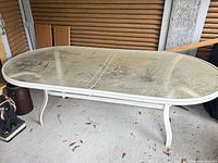 Full view of oval glass patio table showing glass surface and white metal frame