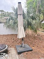 Closed beige patio umbrella on weighted base full view