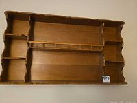 Front view of light brown wall display shelf showing cubbies and spindle plate rack