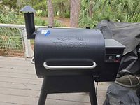 Left front view of Traeger pellet grill showing logo, chimney, handles, control panel