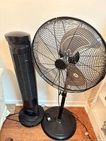 Pedestal fan and tower fan side by side on floor