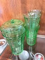 Four tapered green uranium glass ribbed tumblers beside covered dish lid visible