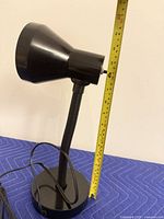 Side view of black metal desk lamp on base with tape measure showing ~13 in height