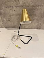 Three-quarter view showing brass cone shade, black frame, clear cord