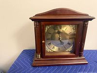Front view showing clock face, glass door, wood case and gold accents