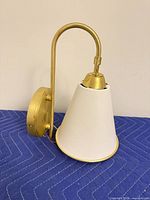 Front side of gold and white wall sconce showing arm, backplate and shade