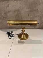 Front view of polished brass piano desk lamp with power cord visible
