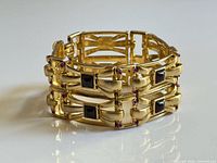 Bracelet standing upright showing triple-row gold links, black square stones and purple rhinestone connectors