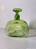 Front view of green Blenko decanter with stopper and foil label visible