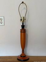 Full view of lamp showing orange wood body, black accents, brass socket and harp