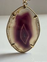 Front view of purple agate slice pendant showing banding and gold-tone frame