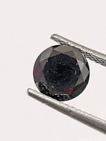 Round faceted black diamond held by tweezers, front view