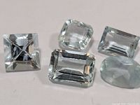 five faceted aquamarine gemstones arranged on white background