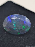 Faceted oval black opal showing green and blue fire