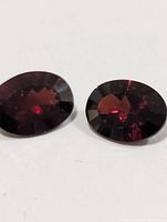 Two oval-cut garnet gemstones viewed from top, showing color and cut