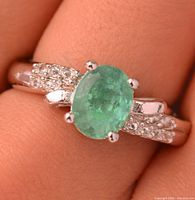 Ring on finger showing emerald and accent stones